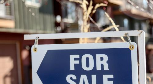 Blue and white for-sale sign pointing at house