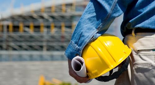 Foreman on construction site holding yellow hard hat with back turned