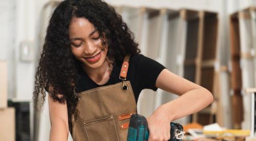 Teenage girl using drill in wood shop class