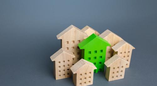 Green model house surrounded by wooden houses with gray background