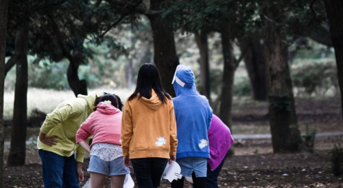 group of five teenagers in park crowd around to look at something on ground