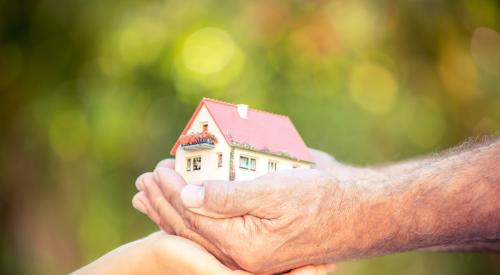 Young hands cupping older hands holding a house