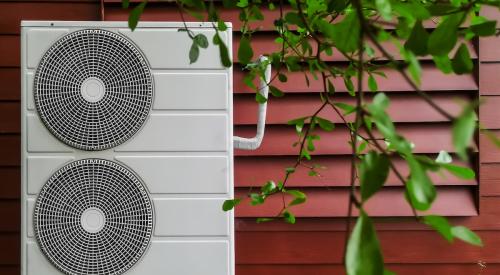 Electric heat pump against exterior wall of red residential home