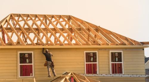 Home builder standing on roof of new house under construction