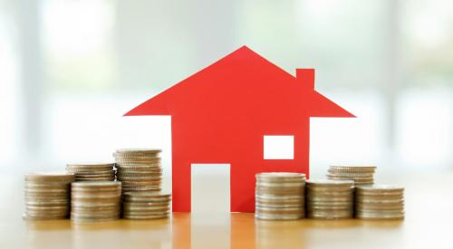 Red paper house in between stacks of coins