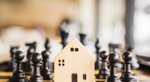 Chess pieces surrounding small wooden house on a chess board