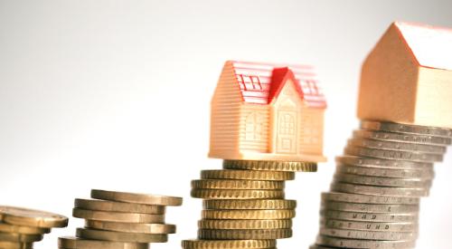 Small toy houses balanced on top of leaning stacks of coins