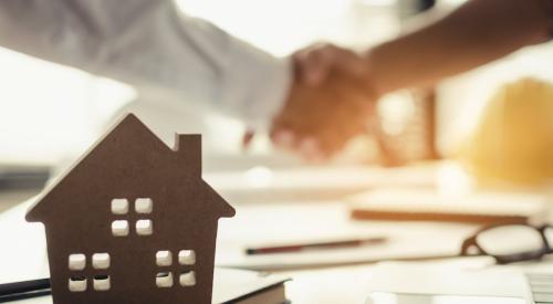 Small wooden house model in front of buyer and seller shaking hands