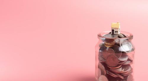 Small house model on top of jar filled with coins with pink background