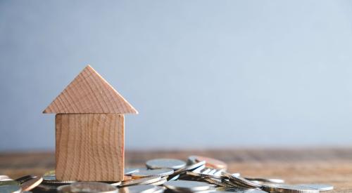 Small wooden house model on top of stack of coins