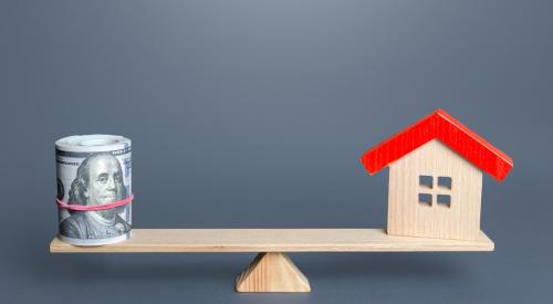 Wooden house with red roof one one end of a teeter totter and a wad of money on the other end balancing