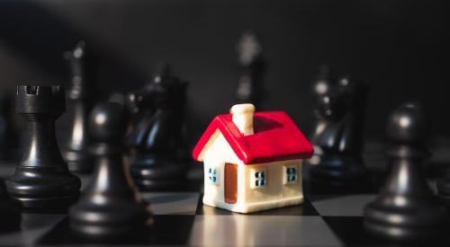 White house model with red roof on chess board surrounded by black chess pieces