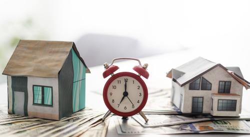 Two houses on top of stacks of money with a clock in between