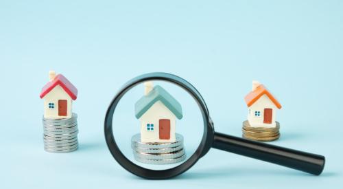 Magnifying glass over small house on top of stack of coins