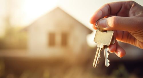 Person holding silver keys with single-family home blurred in background