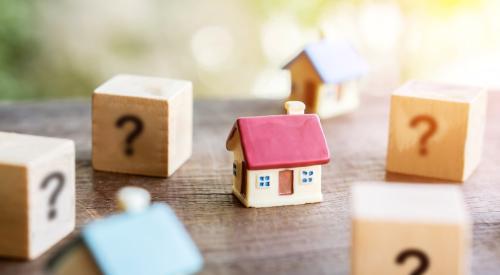 Small house model with red roof surrounded by question marks