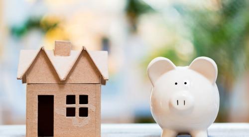 Small wooden house model next to piggy bank