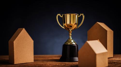 Small wooden house models next to trophy for housing awards