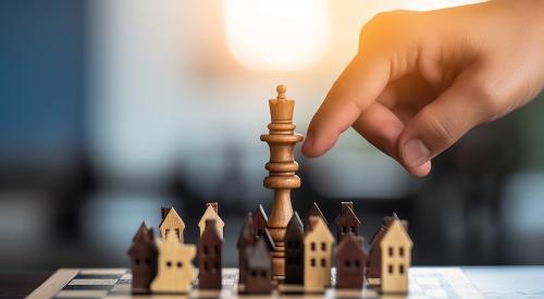 Small wooden houses on chess board being moved by a player