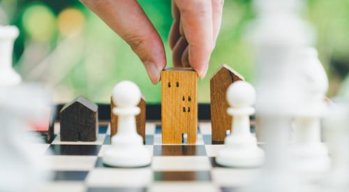 Person moving wooden house on chess board