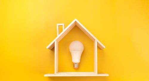 Light bulb inside of small wooden house against yellow background