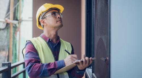 Man wearing a yellow hardhat and using a clipboard inspects a home