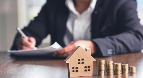 Home model with coin stacks and businessman in background