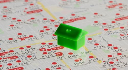 Small green house model on top of map of real estate listings