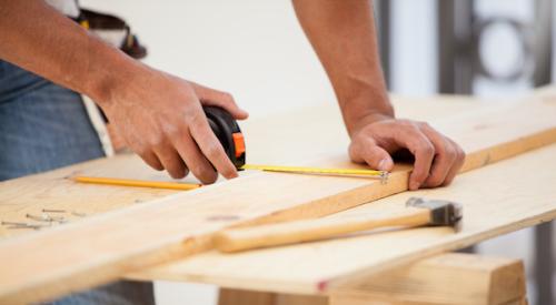 Man using tape measure to measure piece of wood on sawhorse