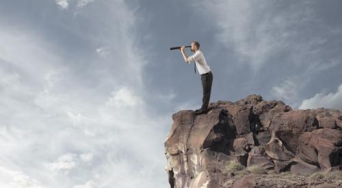 Man on cliff edge looking through spyglass to see what's ahead for his business