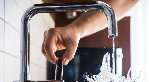 Modern-style kitchen faucet being turned on and splashing water into glass