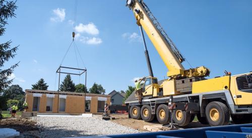 Crane transporting modular home structure to jobsite