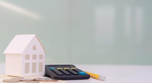 Small white house with stacks of coins, a calculator, and a pencil