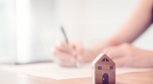 Person signing paper next to small wooden house model