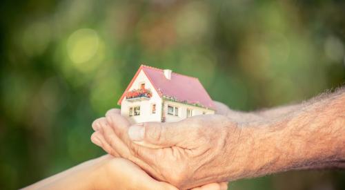 Old and young hands holding multigenerational home model against spring background