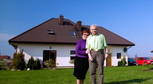 Old couple standing on lawn outside of white residential home