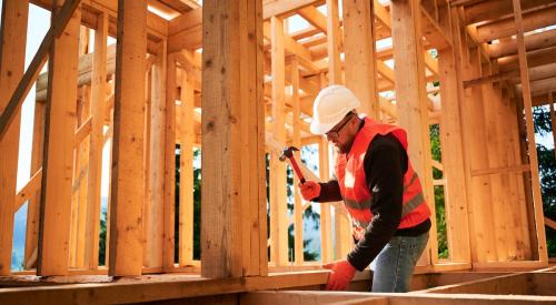 Contractor hammering nail into wood-framed house