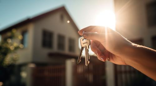 Hand holding up house keys with house in background 