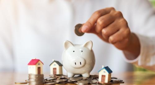 Person dropping coin into piggy bank next to small model houses