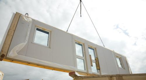 Prefab wall panel being lowered into place by a crane on a jobsite