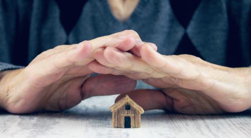 Person holding hands over small wooden house