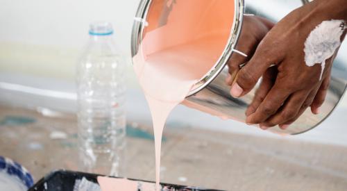 Person pouring peach paint into paint tray with roller