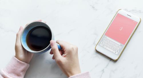 Person holding mug of coffee with smart phone out