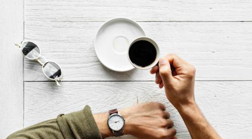 Person at table drinking coffee and checking their watch