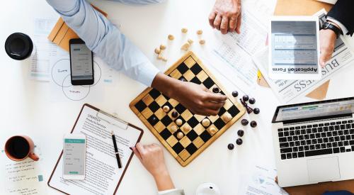 People playing chess on table with laptops and papers