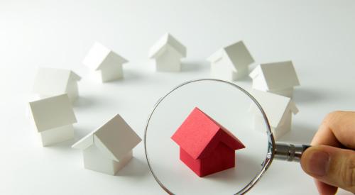 Red house under magnifying glass surrounded by white houses