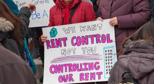 Protestor holding sign that reads "We want rent control, not you controlling our rent." 