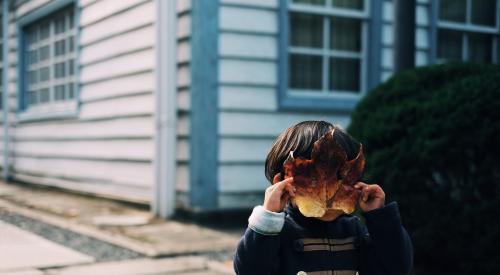 Little kid with maple leaf mask over face in front of house