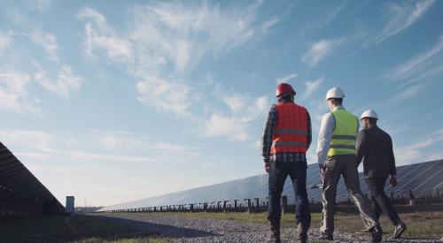 Three men with hard hats walking through solar field