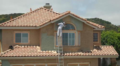 Builder on ladder adding stucco to home exterior